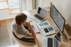 Top wide angle shot of a man doing research in front of his desktop with two laptops on each side