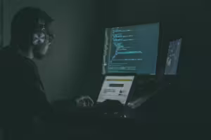 Person doing programming work in a dark room, with A main monitor and laptop 